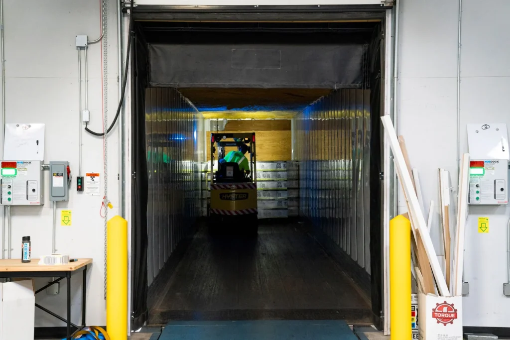 Montacargas entrando a la caja de un trailer sobre el nivelador de anden, con tablero de control y semaforo