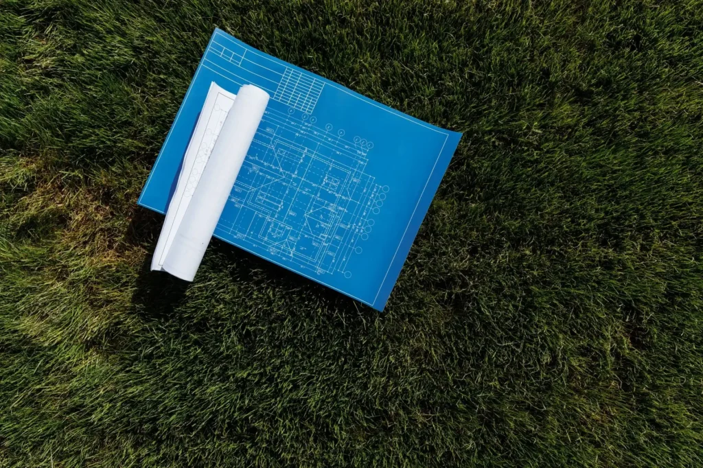 Plano de construccion extendido sobre el pasto de un terreno, antes de iniciar el proyecto